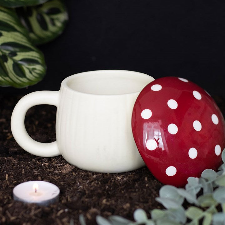 A white ceramic mug with a red mushroom-shaped lid and dots pattern on the lid which is laid on its side 