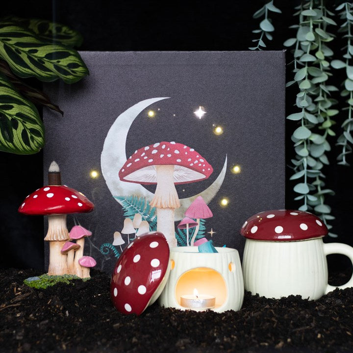 A collection of fantasy-themed home décor items including a canvas print with whimsical moon and mushrooms design, a ceramic mug with a similar design, and other small decorative items arranged on a dark background.