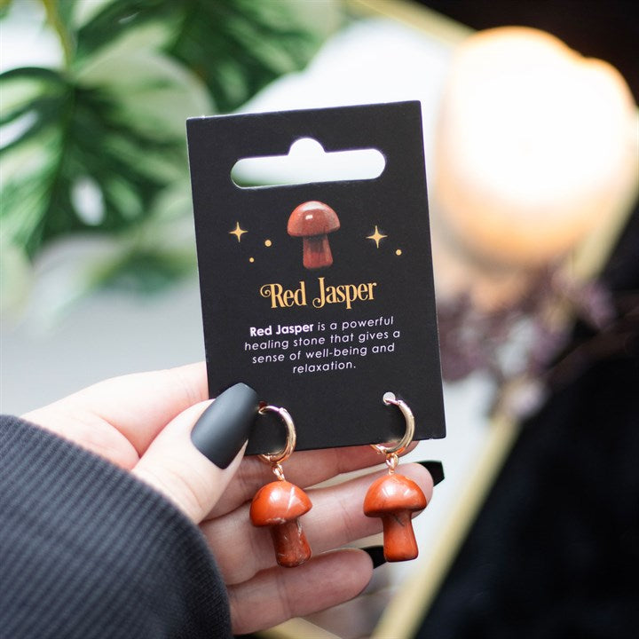 Mushroom shaped red jasper earrings on a black card being held in a hand