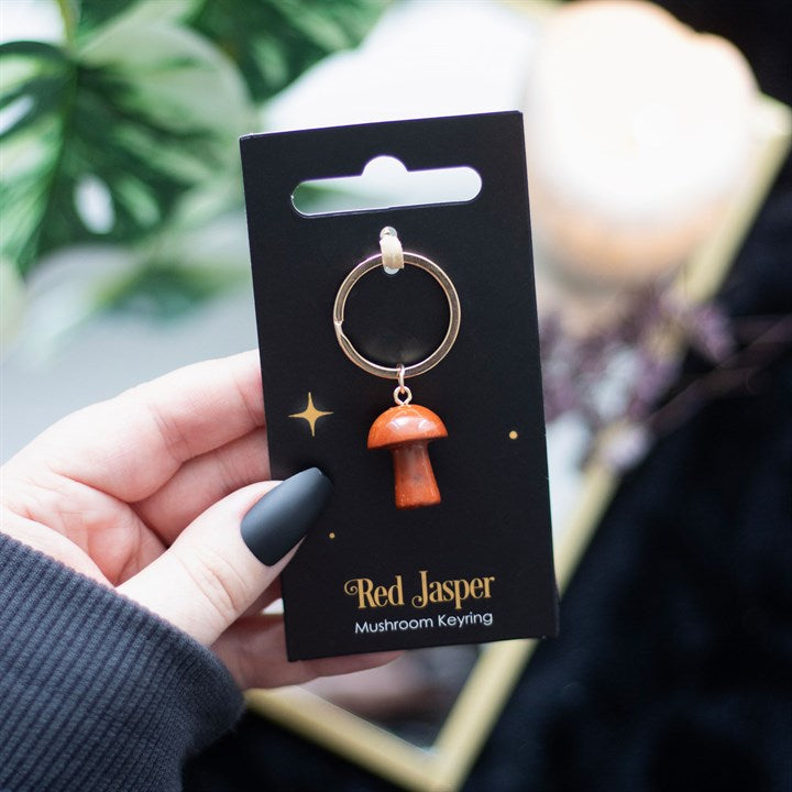 A mushroom shaped red jasper key ring on a black card being held in a hand