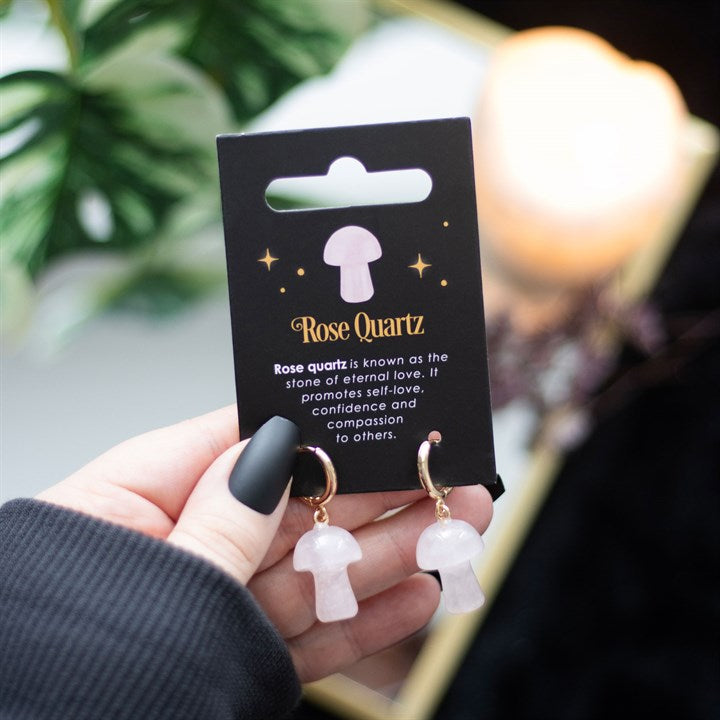 Mushroom shaped rose quartz earrings on a black card being held in a hand