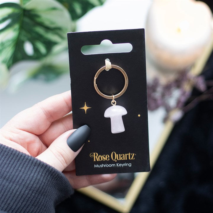 A mushroom shaped rose quartz key ring on a black card being held in a hand