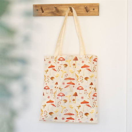 A beige mushroom themed tote bag hanging on a wooden coat hook