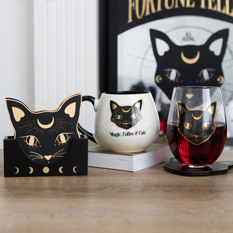 A display of mystical cat themed accessories including a glass, mug, artwork and coasters.