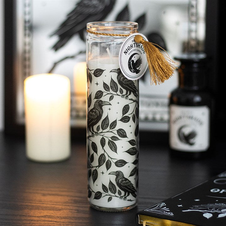 Decorative candle with raven and leaf pattern in a glass jar on a dark surface.