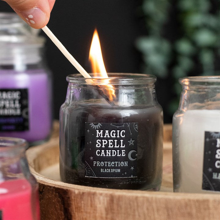 A small lit black Magic Spell Candles with a label that states it is for "Protection" and is Black Opium