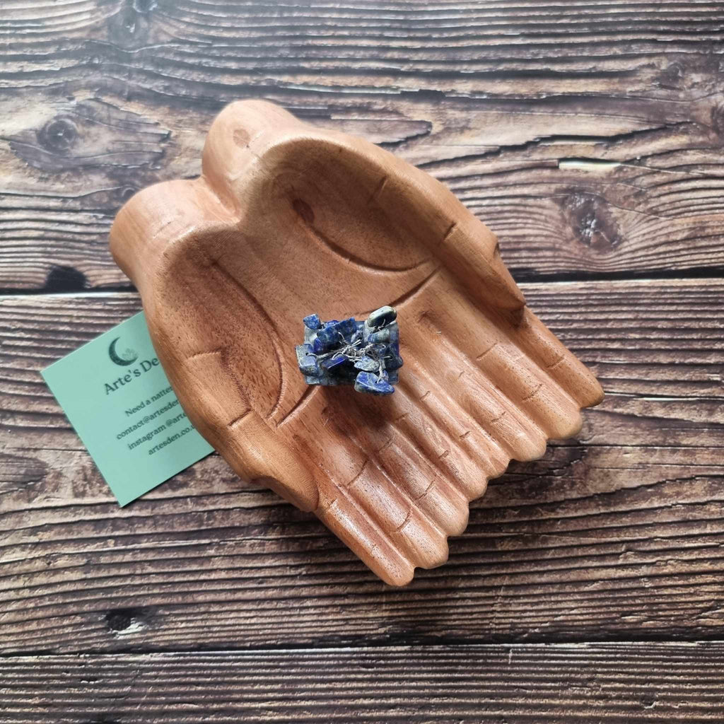 A mini sodalite tree on an orgonite base, displayed on a pair of wooden hands on a wooden surface with an Arte's Den business card