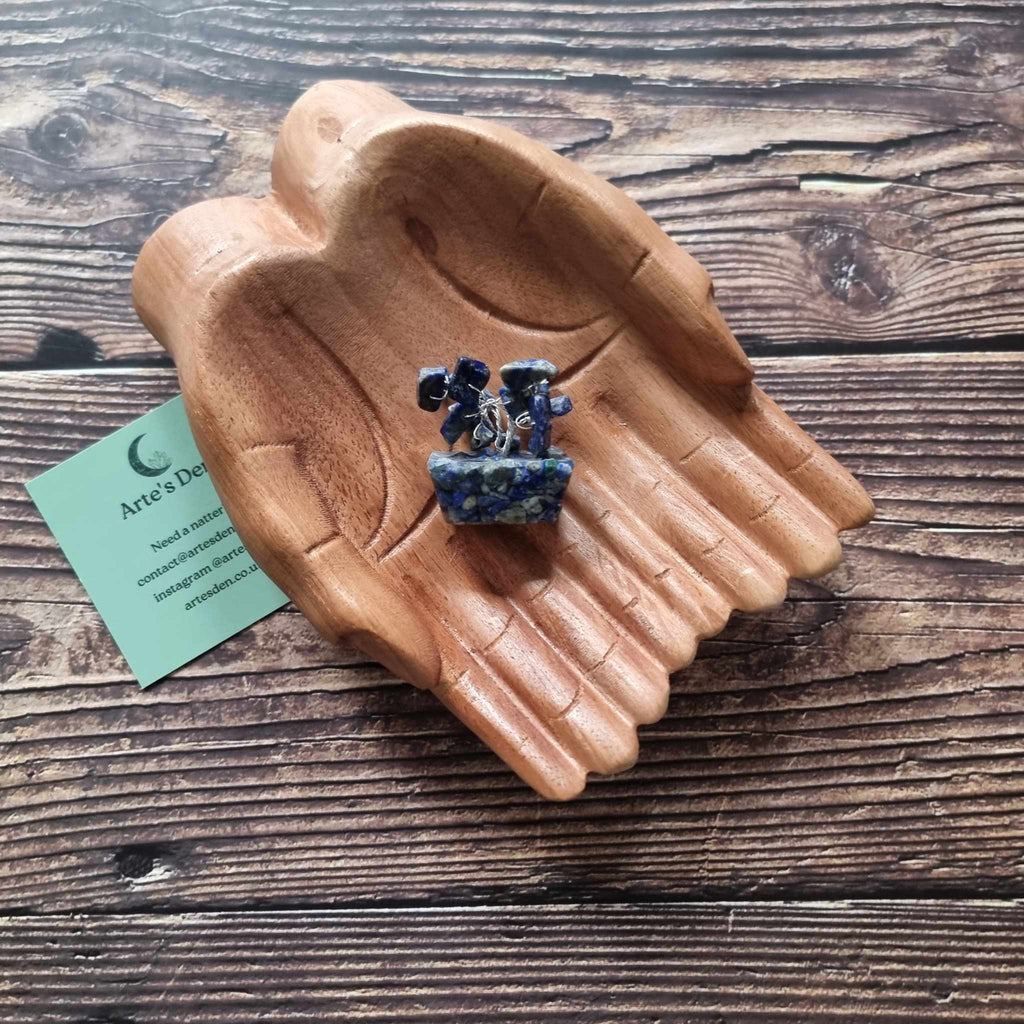 A mini sodalite tree on an orgonite base, displayed on a pair of wooden hands on a wooden surface with an Arte's Den business card