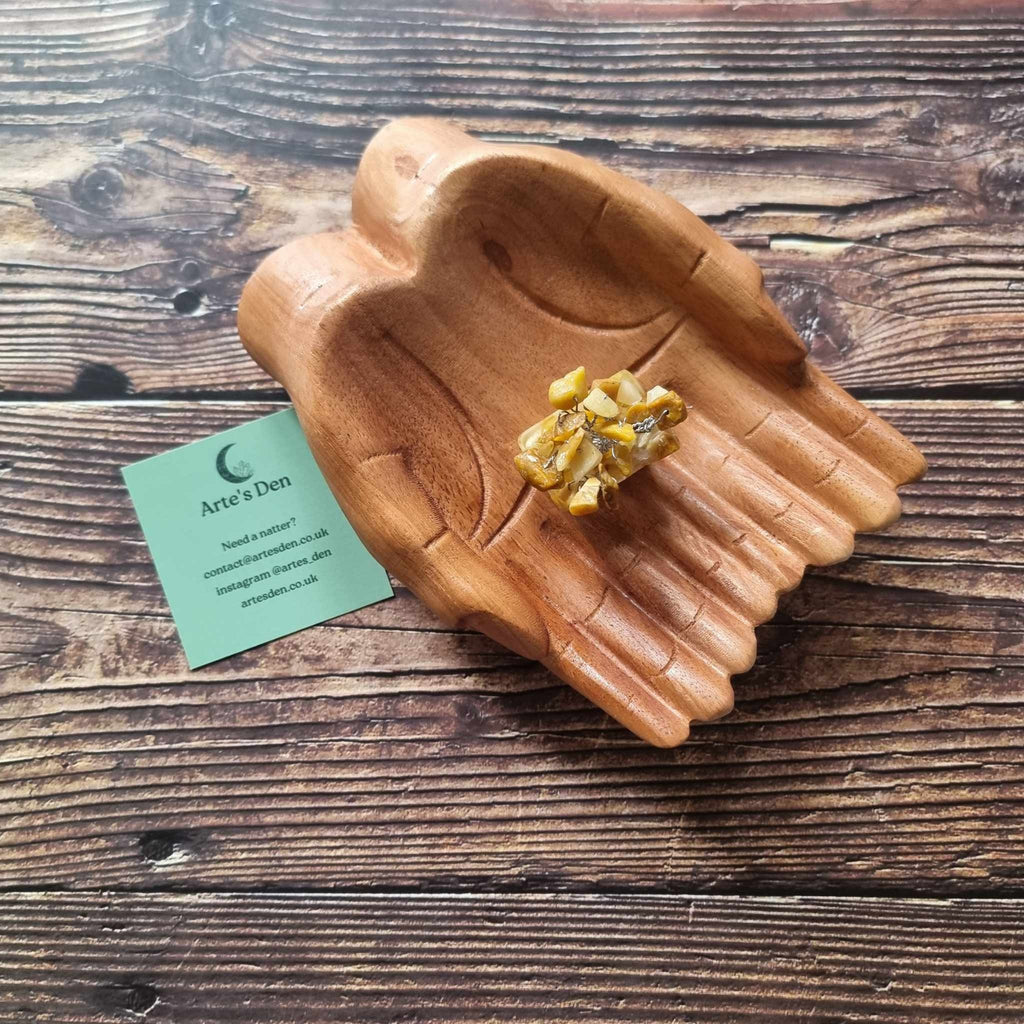 A mini yellow jasper tree on an orgonite base, displayed on a pair of wooden hands on a wooden surface with an Arte's Den business card