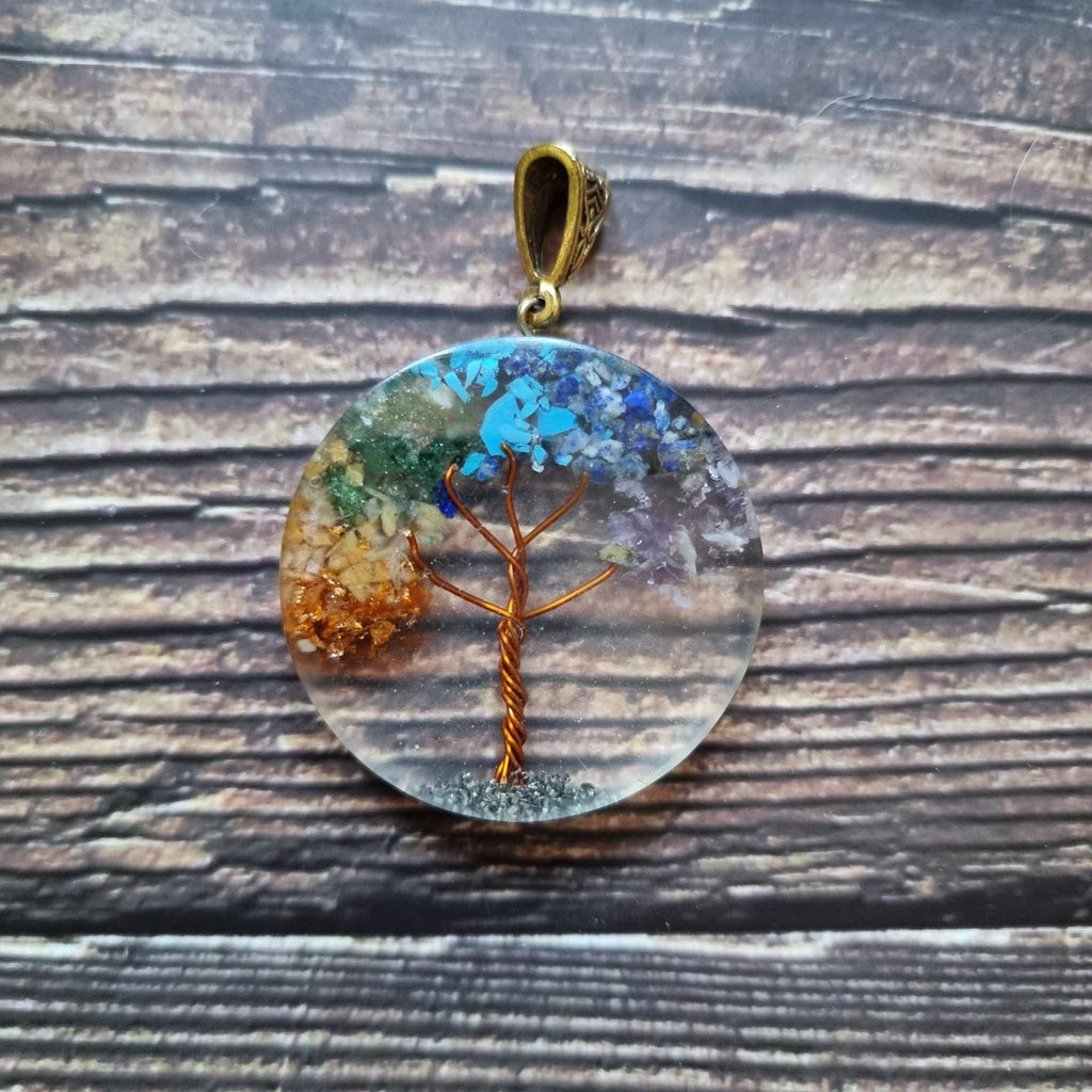 An Orgonite Tree of Life power pendant displayed on a wooden surface, with varying colours