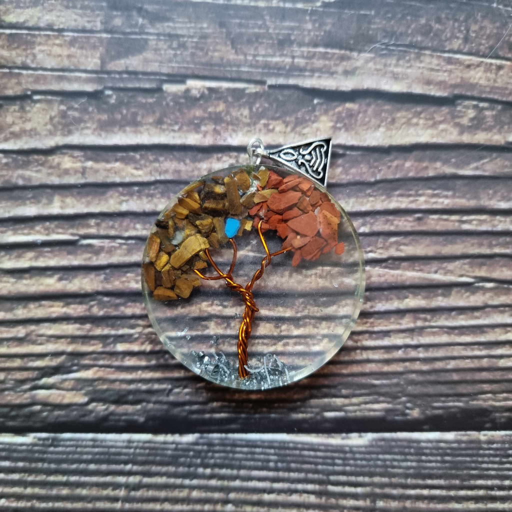 An Orgonite Tree of Life power pendant displayed on a wooden surface, with varying colours