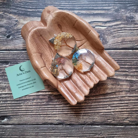 Three Orgonite Tree of Life power pendants displayed in a pair of wooden hands, with varying colours