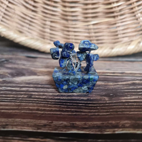 A mini sodalite crystal tree on an orgonite base, with a mix of medium to dark blue and white veins, displayed against a woven background.