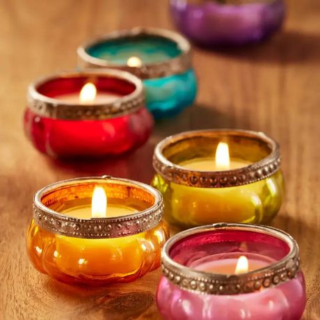 Colourful glass pumpkin shaped tea light holders on a wooden surface