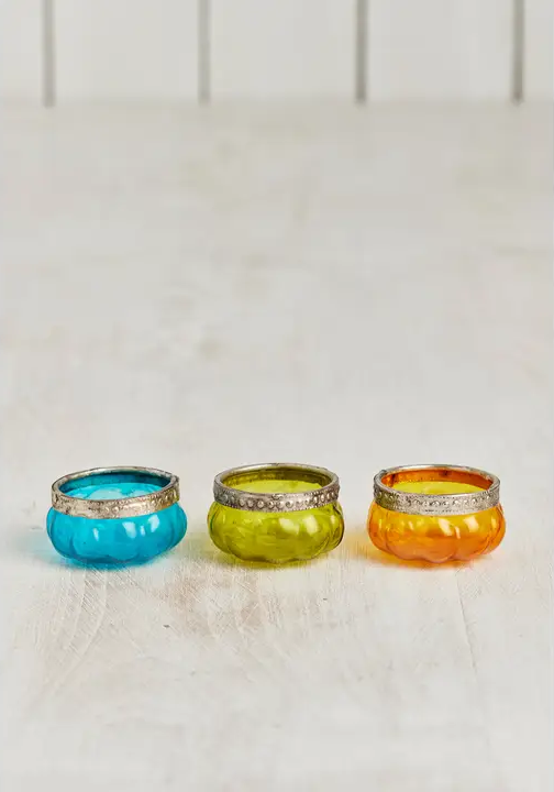 Three Colourful glass pumpkin shaped tea light holders on a white surface