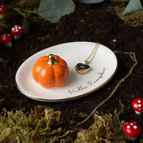 Small pumpkin-shaped trinket dish and heart necklace on a white plate with 'Hello Pumpkin' text, surrounded by autumn-themed decor.
