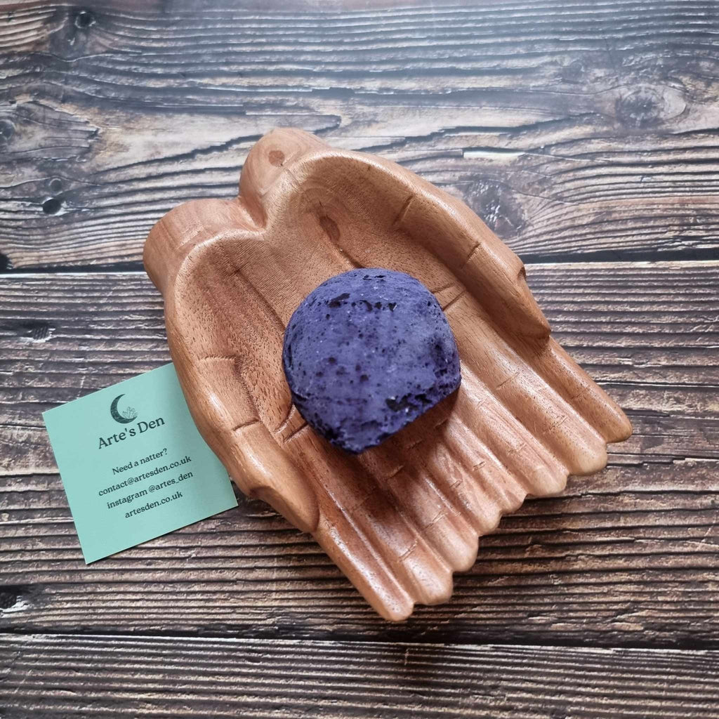 A purple agate geode displayed in a wooden hand-shaped dish with a business card beside it, on a wooden background.
