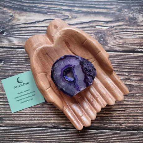 A purple agate geode displayed in a wooden hand-shaped dish with a business card beside it, on a wooden background.