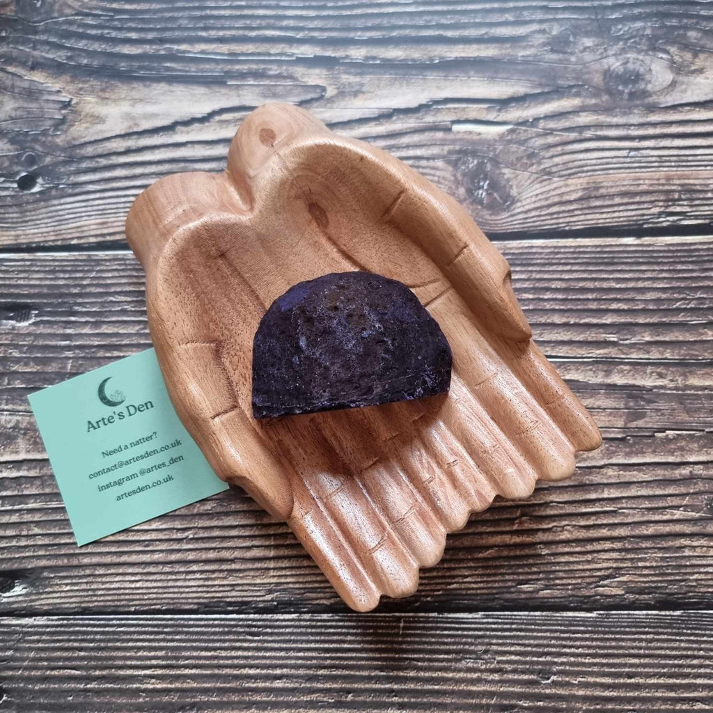 A purple agate geode displayed in a wooden hand-shaped dish with a business card beside it, on a wooden background.