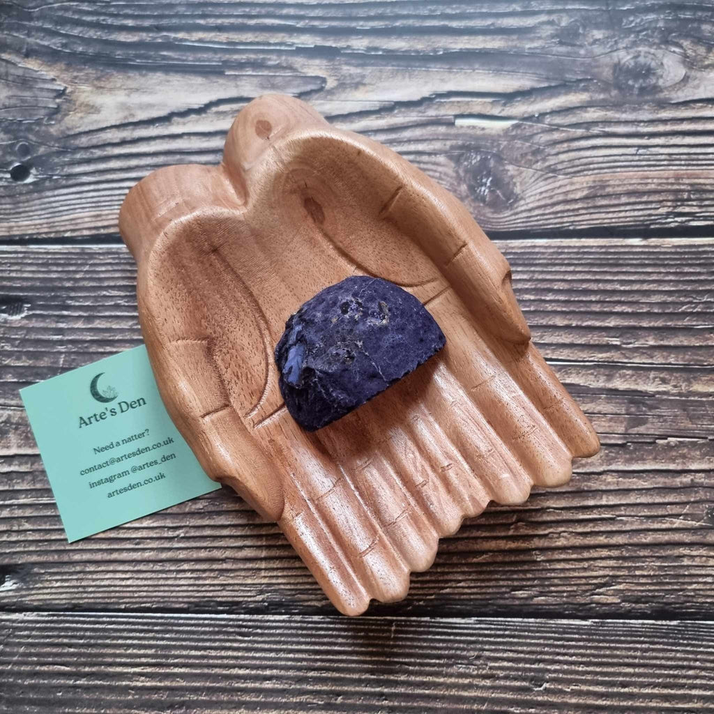 A purple agate geode displayed in a wooden hand-shaped dish with a business card beside it, on a wooden background.