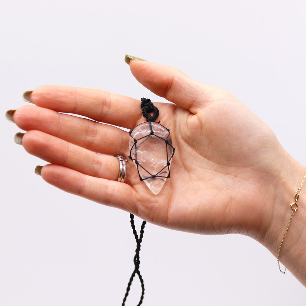 A hand holding a black necklace with a tear shaped quartz crystal pendant  