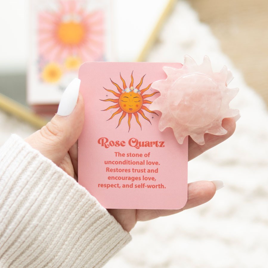A carved Rose Quartz crystal sun alongside a card explaining about Rose Quartz. Held in a hand.