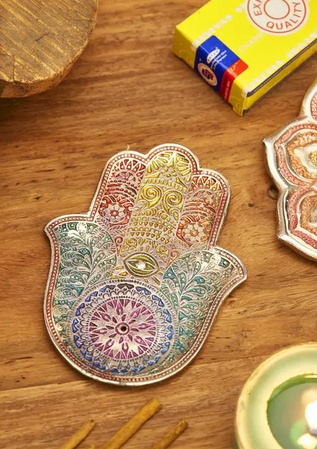 Decorative Hamsa hand incense holder on a wooden surface with a box of incense in the background.
