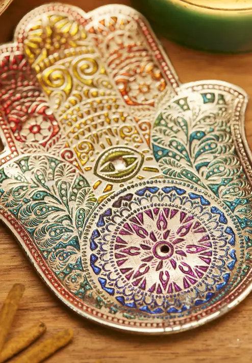 Colourful Hamsa incense holder with intricate patterns on a wooden surface