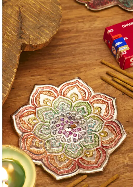 Decorative mandala incense holder on a wooden surface with candles and cards.