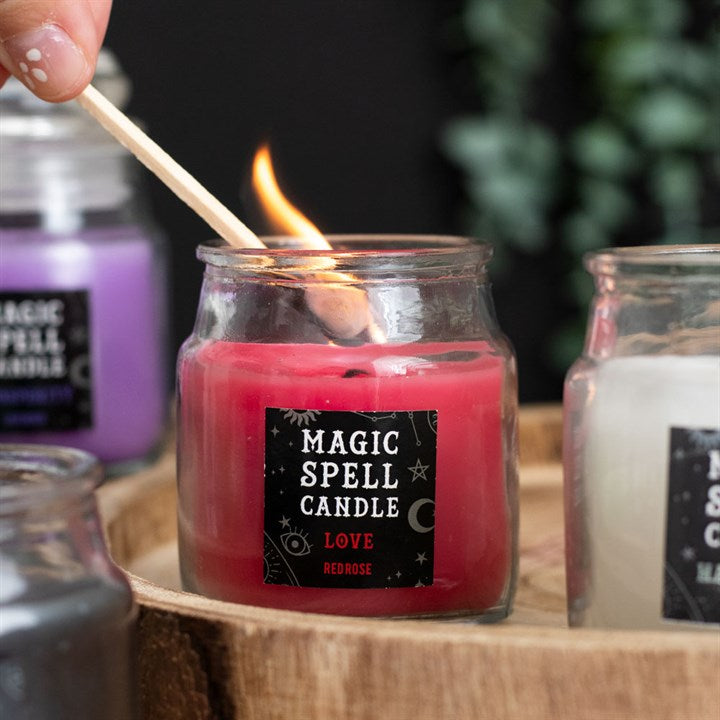 A small lit red Magic Spell Candles with a label that states it is for "Love" and is Red Rose