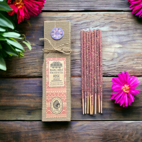 A set of resin incense sticks tied with a string, alongside a beige-coloured ritual resin packaging with decorative patterns and text, placed on a wooden surface with flowers.