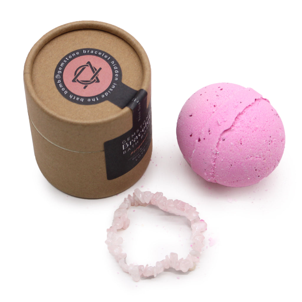 A brown package with black label stating "gemstone bracelet bath bomb" next to a pink bath bomb and rose quartz bracelet on a white background. 