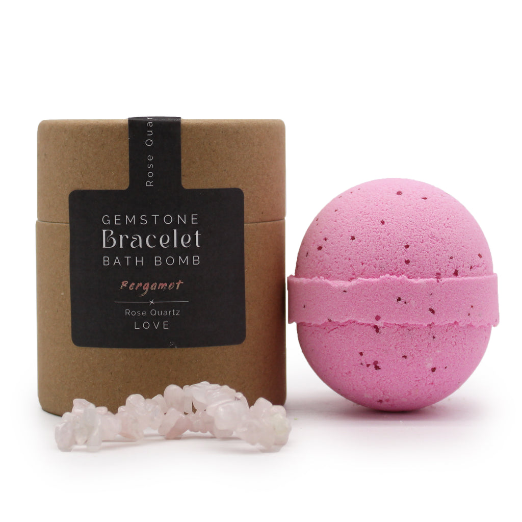 A brown package with black label stating "gemstone bracelet bath bomb" next to a pink bath bomb and rose quartz bracelet on a white background. 