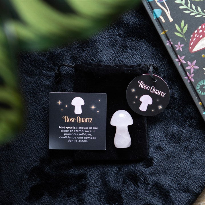 A Rose Quartz mushroom crystal placed on a dark fabric, with a drawstring bag and a card that has 'Rose Quartz' text next to it.