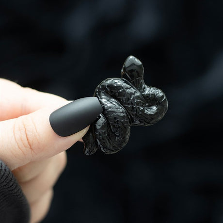 A close-up image of a black obsidian snake-shaped crystal carving held by a person with a dark background.