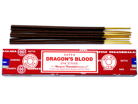 A pack of Satya incense sticks with the label 'DRAGON'S BLOOD' displayed on the packaging. The sticks are shown both in and out of the packaging, revealing dark coloured incense with gold accents on the ends.