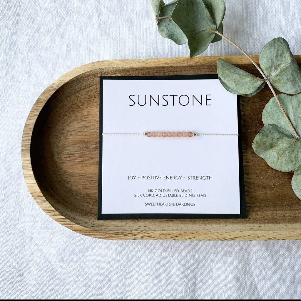 A Sunstone silk bracelet with beads approximately 3mm in size, displayed on a wooden tray alongside a keepsake card that reads 'Sunstone - JOY - POSITIVE ENERGY - STRENGTH'
