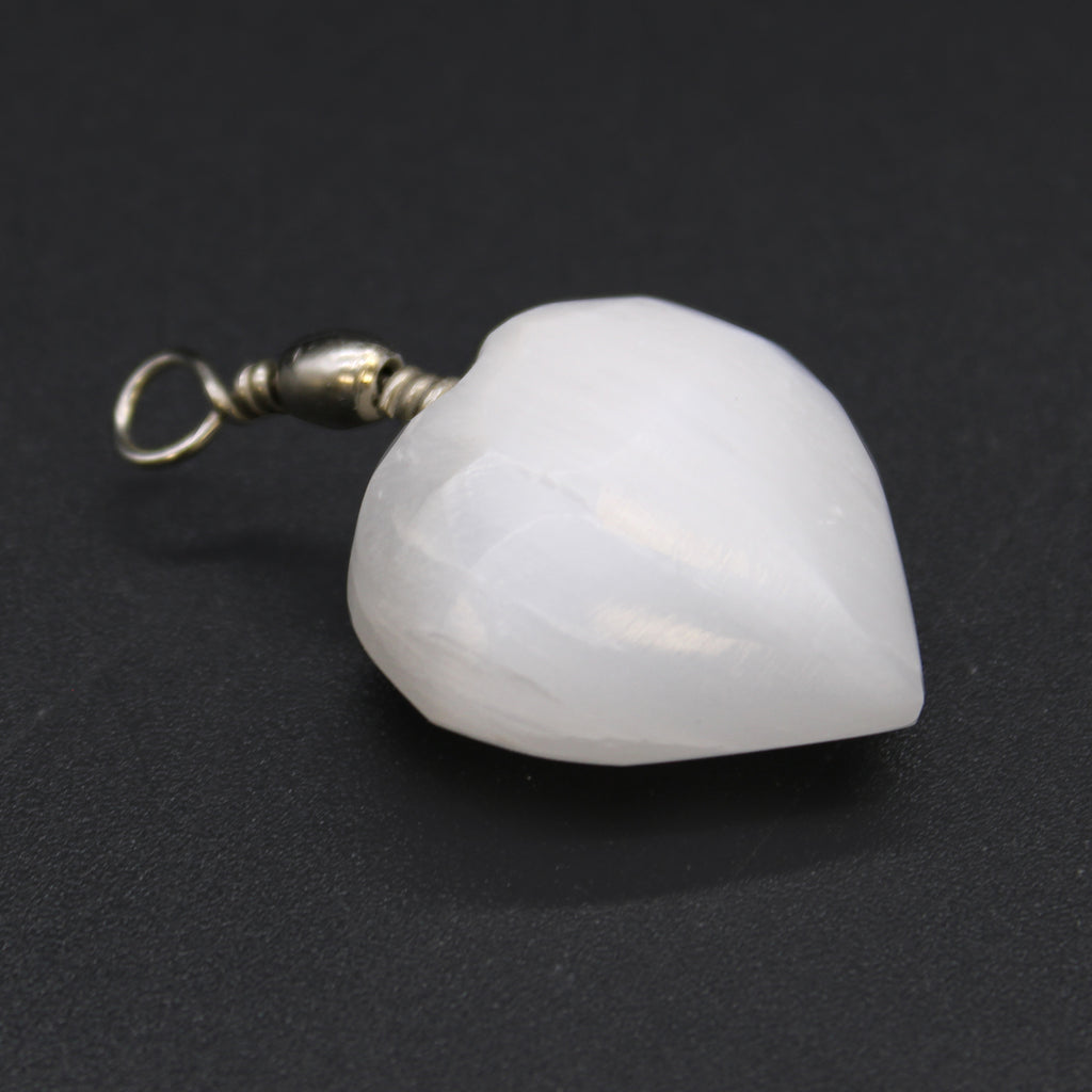 A close up of a Selenite heart pendant against a black background