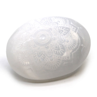 A Selenite oval, carved with intricate mandala design, laid on a white background