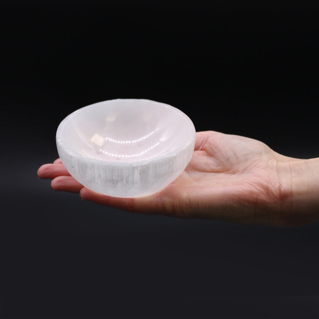A white selenite bowl, held in a hand on with a black background