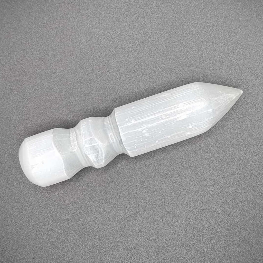 Image of a selenite wand which is a milky colour, pointed at one end and grooved near the other end.