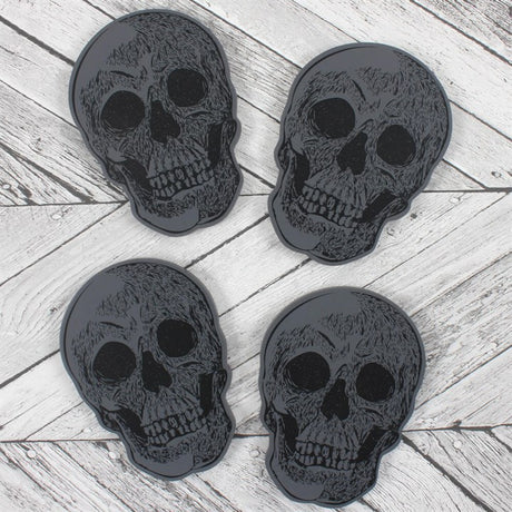A set of four black skull-shaped coasters on a wooden surface.