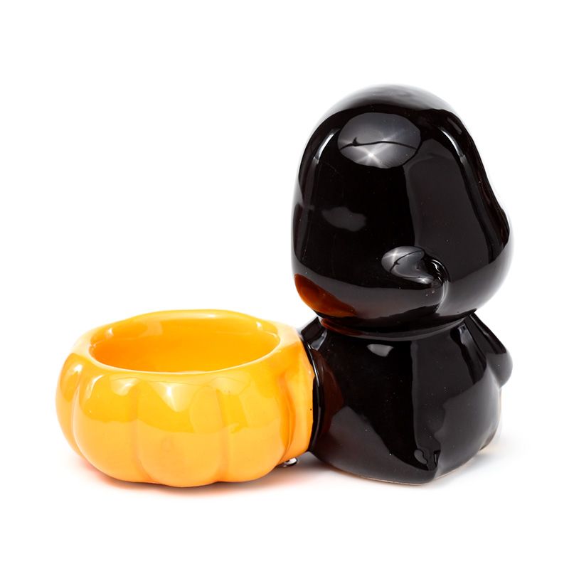Black skeleton figure with a yellow jack-o'-lantern tea light holder from behind on a white background 