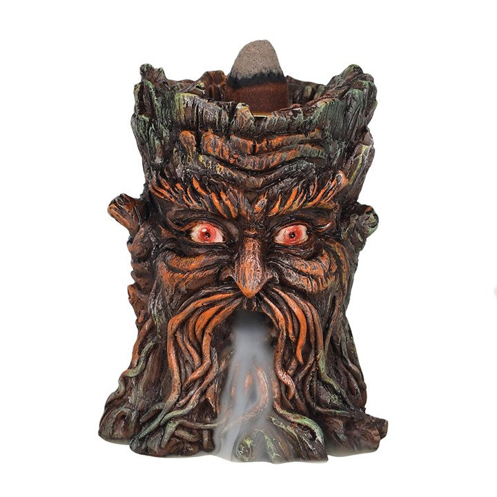 A brown resin Green Man backflow incense burner with smoke cascading downwards, placed on a white surface
