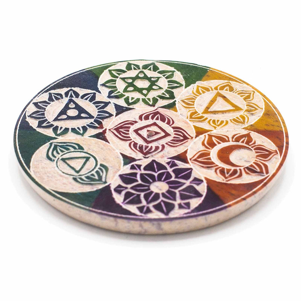 A colourful soapstone incense holder with chakra symbols, placed on a white surface