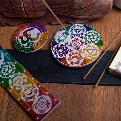 A colourful soapstone incense holder with chakra symbols, alongside incense sticks and a holder, placed on a dark surface.