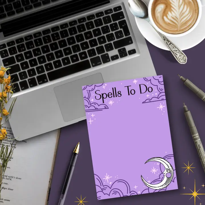 Purple notepad titled 'Spells To Do' on a desk with a laptop, coffee, and stationery.
