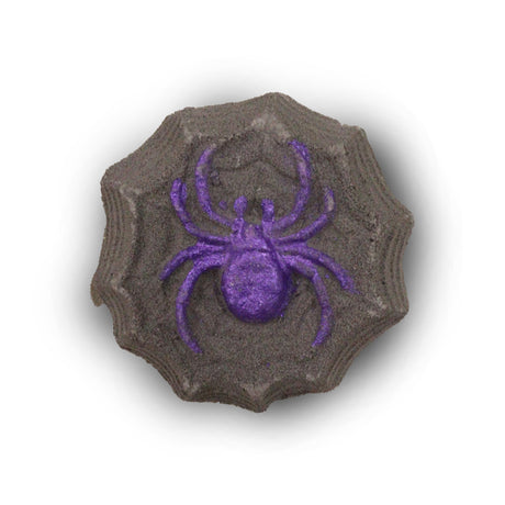 A black bath bomb in the shape of a spiders web with a purple spider in the middle on a white background. 