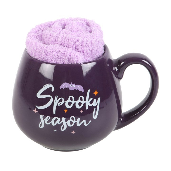A purple ceramic mug with the text 'Spooky Season' written on it, holding a pair of lilac fluffy socks.