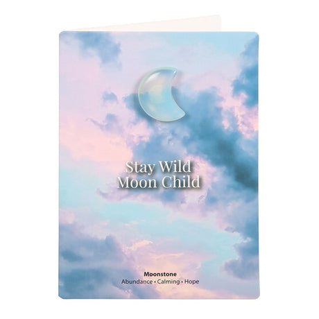 A greeting card with a crescent moon design and the text 'Stay Wild Moon Child'. The background features a soft blend of blue and purple hues, resembling a sky at dusk.